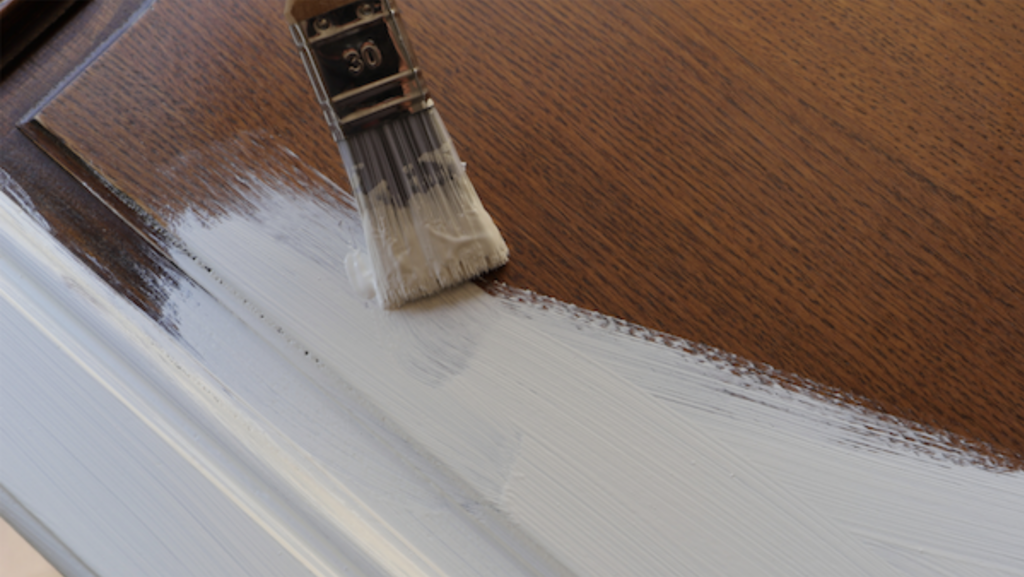 A paintbrush with white chalk paint painting wood